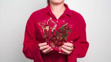 mujer sosteniendo un sobre rojo chino con conejo dorado y palabra de bendición, regalo de dinero para felices vacaciones de año nuevo lunar. frase china significa felicidad, salud, suerte y riqueza video