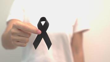 mujer con cinta negra para melanoma y cáncer de piel, mes de concientización sobre lesiones por vacunas, dolor y descanso en paz. salud y concepto racista video