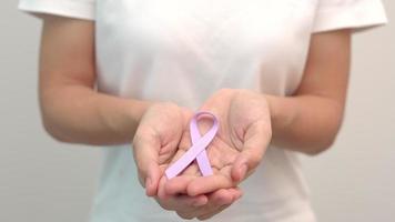 día mundial contra el cáncer, 4 de febrero. mano de mujer sosteniendo cinta púrpura lavanda para apoyar a las personas que viven y están enfermas. concepto médico y de salud video