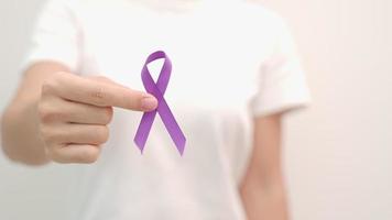 mano que sostiene la cinta morada para el cáncer de páncreas, esófago, testículo, alzheimer mundial, epilepsia, lupus, sarcoidosis, fibromialgia y mes de concientización sobre la violencia doméstica. concepto del día mundial del cáncer video