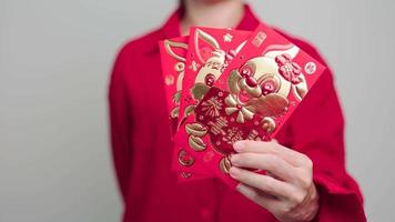 mujer sosteniendo un sobre rojo chino con conejo dorado y palabra de bendición, regalo de dinero para felices vacaciones de año nuevo lunar. frase china significa felicidad, salud, suerte y riqueza video