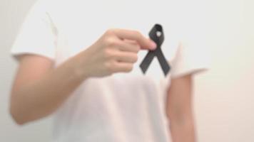mulher segurando fita preta para melanoma e câncer de pele, mês de conscientização de lesões por vacina, luto e descanse em paz. saúde e conceito racista video