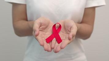 Hand holding Red Ribbon for December World Aids Day, acquired immune deficiency syndrome, multiple myeloma Cancer Awareness month and National Red ribbon week. Healthcare and world cancer day video