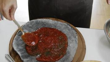 aplicar ketchup con cuchara de metal sobre base de pizza