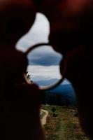 The bride and groom hold a ring in their lips, mountains can be seen through the ring. photo