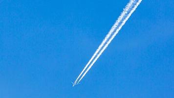 Two engined airplane during flight in high altitude with condensation trails photo