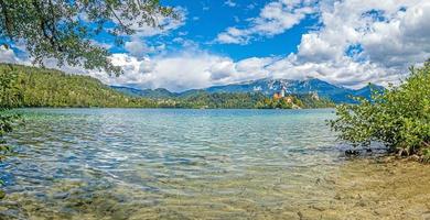 View of Bled castle and pilgrimage church with the Alps in the background in Slovenia during the day photo