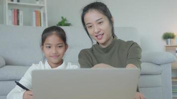 Mother teaching lesson for daughter by laptop. Asian young little girl learn at home. Do homework with kind mother help, encourage for exam. Asia girl happy Homeschool. Mom advise education together.
