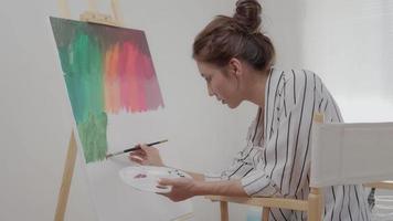 la artista femenina profesional usa pincel en el arte abstracto para crear una obra maestra. pintura de pintor con acuarelas o aceite en casa de estudio. bella mujer disfruta pintando como hobby. recreación laboral video