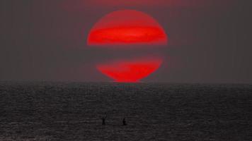 Time lapse of a red sun sunset in the sea. Picturesque seascape in the evening at sunset. People silhouettes sun background. Tourism and travel concept video