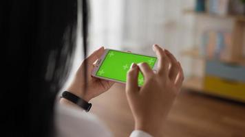 Closeup horizontal of hand woman using smartphone with green screen while lying on couch. Blank digital smartphone in hand girl. Showing content videos blogs tapping on center screen.