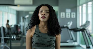 Handheld Portrait shot, Young beautiful woman wiping sweat with tired after finishes exercise in gym, Curly hair woman in sportswear looking at camera video