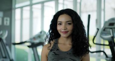 Handheld Portrait shot, Young beautiful Curly hair woman in sportswear smile and looking at camera in exercise gym