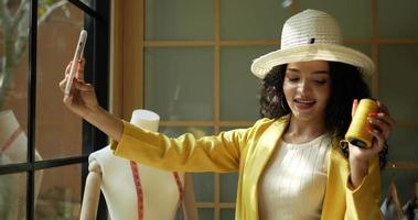 gros plan de poche, belle jeune designer portant un chapeau de mode élégant et utilisant un appel vidéo sur smartphone montrant un fil jaune et rouge avec bonheur dans une boutique de tailleur