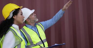 Handheld panning shot, middle-aged Caucasian business engineer man and pretty secretary female checking transport container, They are talking and write into report paper on clipboard at storage video