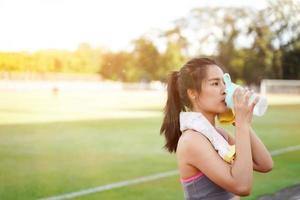 mujer joven relajándose y bebiendo agua después del entrenamiento físico en el estadio de fútbol por la mañana. foto