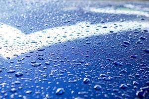 fondo y textura de gotas de lluvia e iluminación de reflexión sobre el capó del motor de coche azul.