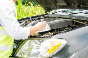 Closeup and crop Insurance agent writing on clipboard while examining car after accident claim being assessed and processed on car engine background. photo