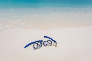 Summer beach coastline snorkel gear, googles on soft sand calm waves splashing. Tropical summer shore closeup, freedom adventure, outdoor recreation. Relaxing view of recreational activity, snorkeling photo