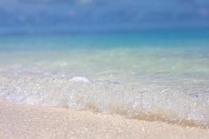 mar tropical y arena bajo el cielo azul. paisaje de playa tropical. suave ola azul del océano en una playa de arena limpia. fondo de las olas del océano. arena blanca y mar azul cristalino. océano agua naturaleza, playa relax foto