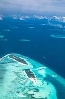 Aerial view of Maldives resort, luxury travel destination. Birds eye view of deep blue sea, coral reed, tropical island. Amazing nature view, drone aerial landscape photo