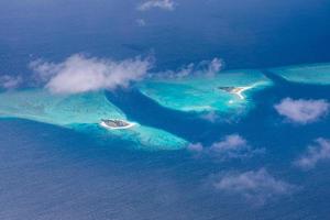 Aerial view of Maldives resort, luxury travel destination. Birds eye view of deep blue sea, coral reed, tropical island. Amazing nature view, drone aerial landscape photo