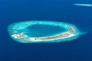 Aerial view of Maldives resort, luxury travel destination. Birds eye view of deep blue sea, coral reed, tropical island. Amazing nature view, drone aerial landscape photo