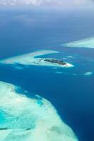 Aerial view of Maldives resort, luxury travel destination. Birds eye view of deep blue sea, coral reed, tropical island. Amazing nature view, drone aerial landscape photo