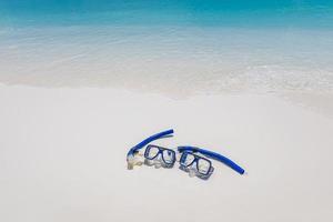 Summer beach coastline snorkel gear, googles on soft sand calm waves splashing. Tropical summer shore closeup, freedom adventure, outdoor recreation. Relaxing view of recreational activity, snorkeling photo