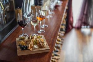 selección de vinos y set de snacks. variedad de queso, aceitunas, prosciutto, rodajas de baguette asadas, uvas en una elegante tabla de madera en un interior de lujo foto