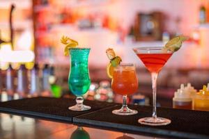 Exotic cocktails, mojito cocktail, orange cocktail, strawberry cocktail in glass glasses with straws and fruits and blurred bar accessories shaker, spoon, spices Colorful cocktails on the bar counter photo