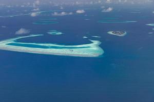 Aerial view of Maldives resort, luxury travel destination. Birds eye view of deep blue sea, coral reed, tropical island. Amazing nature view, drone aerial landscape photo