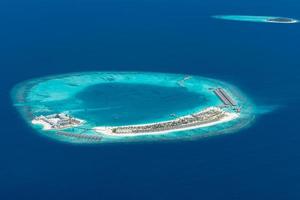 Aerial view of Maldives resort, luxury travel destination. Birds eye view of deep blue sea, coral reed, tropical island. Amazing nature view, drone aerial landscape photo