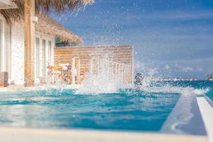 Couple having fun at the swimming pool. Man jumping into infinity pool in luxury resort with water splash over woman face and hair. Funny photo, summer honeymoon, fun outdoors activity photo