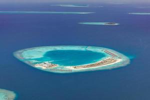 Aerial view of Maldives resort, luxury travel destination. Birds eye view of deep blue sea, coral reed, tropical island. Amazing nature view, drone aerial landscape photo