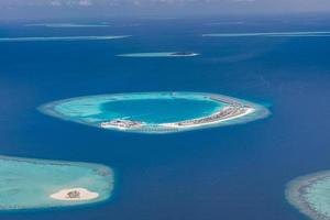 Aerial view of Maldives resort, luxury travel destination. Birds eye view of deep blue sea, coral reed, tropical island. Amazing nature view, drone aerial landscape photo