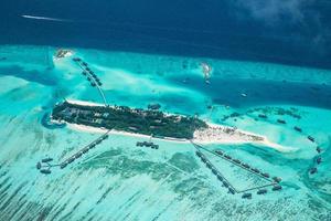 Aerial view of Maldives resort, luxury travel destination. Birds eye view of deep blue sea, coral reed, tropical island. Amazing nature view, drone aerial landscape photo