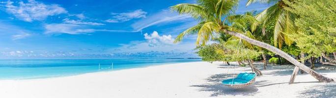 Tropical beach panorama as summer landscape with beach swing or hammock and white sand and calm sea for beach banner. Tranquil beach scene vacation and summer holiday concept. Boost up color process photo