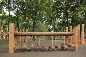 Rope bridge in outdoor modern children wooden playground in a public park of city. Eco-friendly lifestyle rest and childhood concept of safety environmentally infrastructure for kids. Funny adventure photo