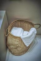 A wicker laundry basket full of fresh white towels on the floor photo