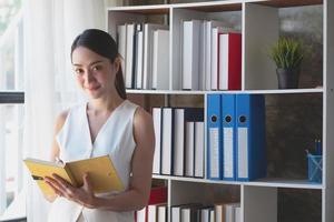 Asian businesswoman presenting business data with a board with charts, graphs hand holding a yellow notebook, And business documents lying on the table in the office, business concept. photo