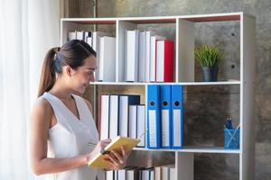 Asian businesswoman presenting business data with a board with charts, graphs hand holding a yellow notebook, And business documents lying on the table in the office, business concept. photo