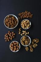 un juego de nueces en tazas blancas sobre un fondo negro. cacahuetes, avellanas y almendras. nuez. un delicioso conjunto de frutos secos. foto