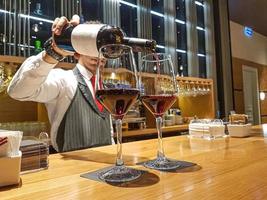 el camarero vierte vino tinto en copas en un mostrador de bar de madera foto