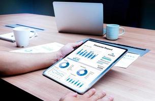 Businessman hand holding tablet with mock up financial report slide show presentation on display in meeting with laptop and coffee cup on table background photo