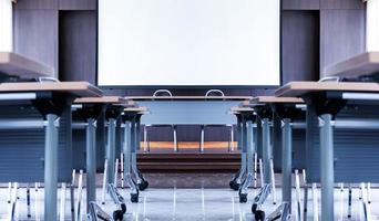 sala de seminarios con una mesa para oradores en medio del escenario y fondo de pantalla blanca