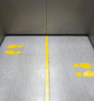 Social distancing for COVID-19 with yellow footprint sign in public elevator