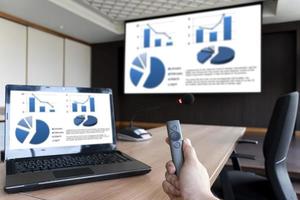 Businessman hand hold remote control with slide presentation on display projector screen and laptop in meeting room photo