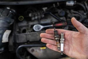 bujía vieja y nueva en manos de un mecánico en el fondo de un motor de camión foto