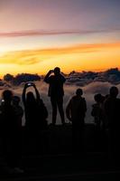 Silhouette person group watching floating sea of clouds,Sea of fog, Sky above clouds,taking cloudscape photos with mobile phones in the morning,sun rising,travel long weekend,Inthanon mountain.